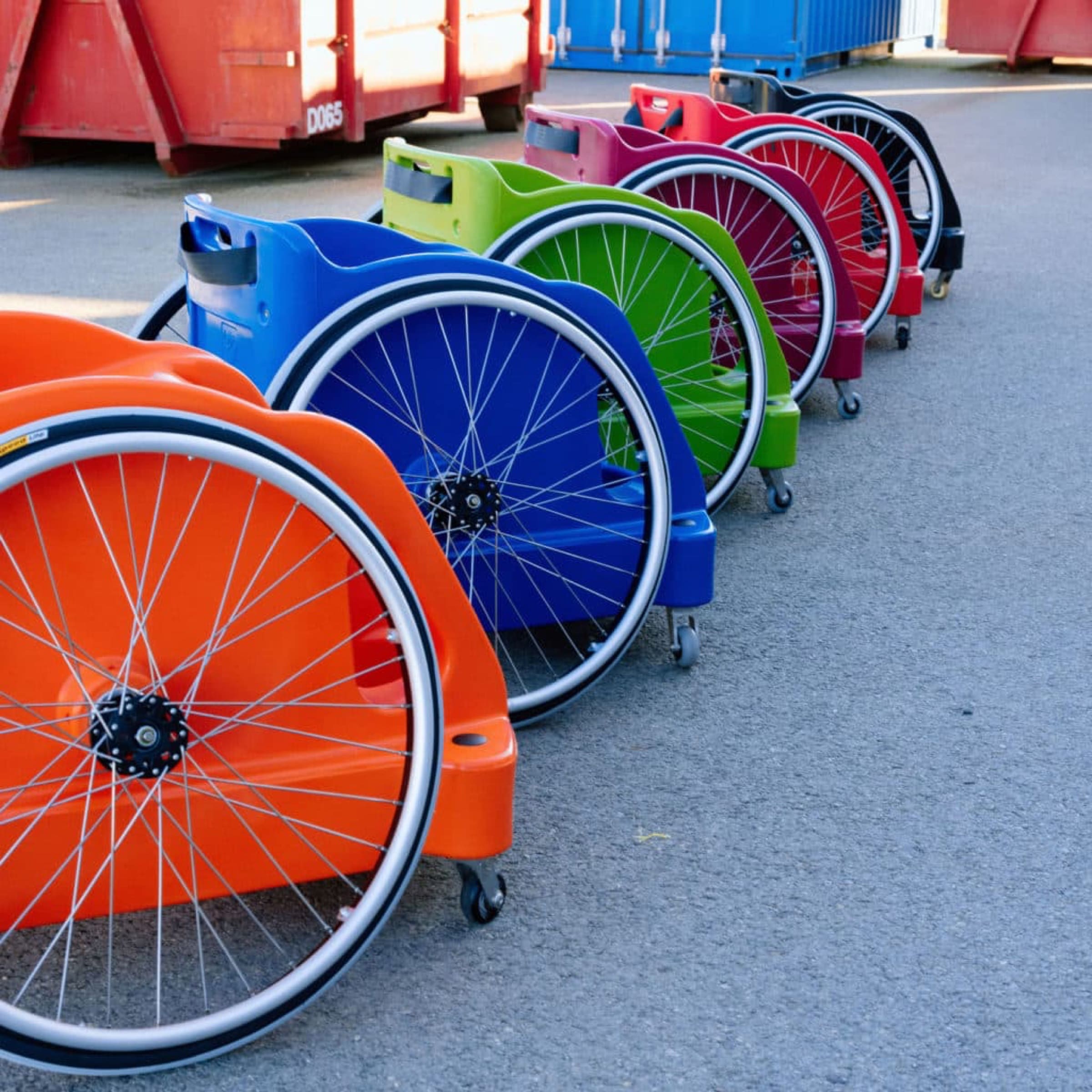 Una fila di carrozzine da rugby dei Romanes dai colori accesi, arancione, blu, verde e rosso, allineate al sole.