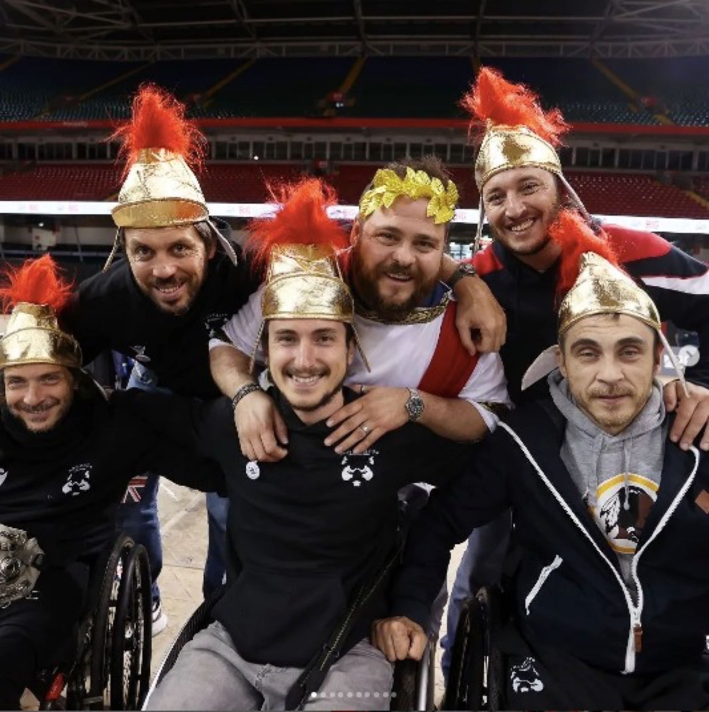 Un gruppo di giocatori dei Romanes, sorridenti e abbracciati, indossa elmi da centurione dorati durante una trasferta.